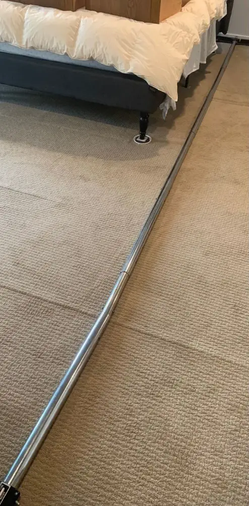 Power stretcher set up on a buckled beige bedroom carpet before re-stretching repair.